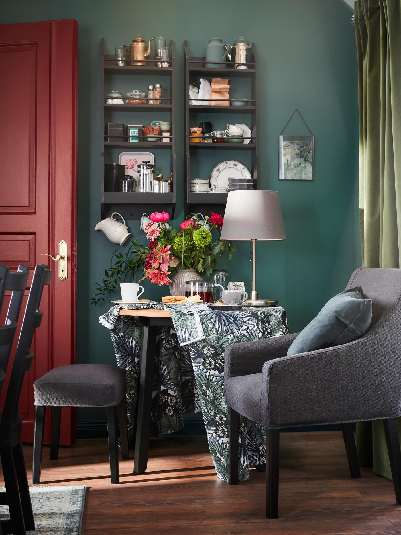 Un colț cu un scaun negru/gri închis cu brațe, o masă unde se servește ceai și o fereastră cu draperii albe/verzi.