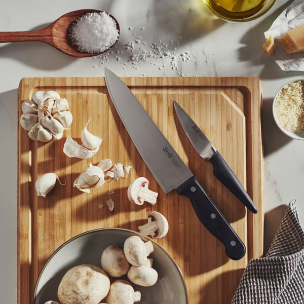 Un coltello da cucina VARDAGEN, un coltello per sbucciare VÖRDA, dell'aglio e una ciotola con funghi su un ceppo per carni in bambù - IKEA.