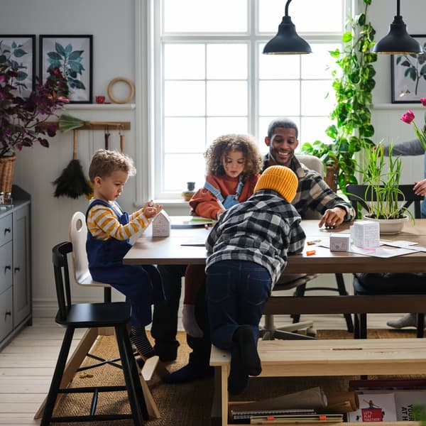 Un comedor con una familia jugando alrededor de una mesa, con sillas y lámparas en una habitación grande, luminosa y amplia.