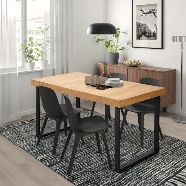Un comedor con una mesa de madera y patas negras con una alfombra de IKEA de lana hecha a mano negra y blanca. Las sillas negras de plástico de IKEA.