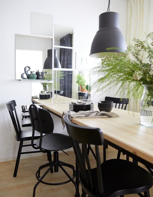 Un comedor cunha mesa de piñeiro e seis cadeiras negras e unha parede decorada con espellos para crear profundidade.