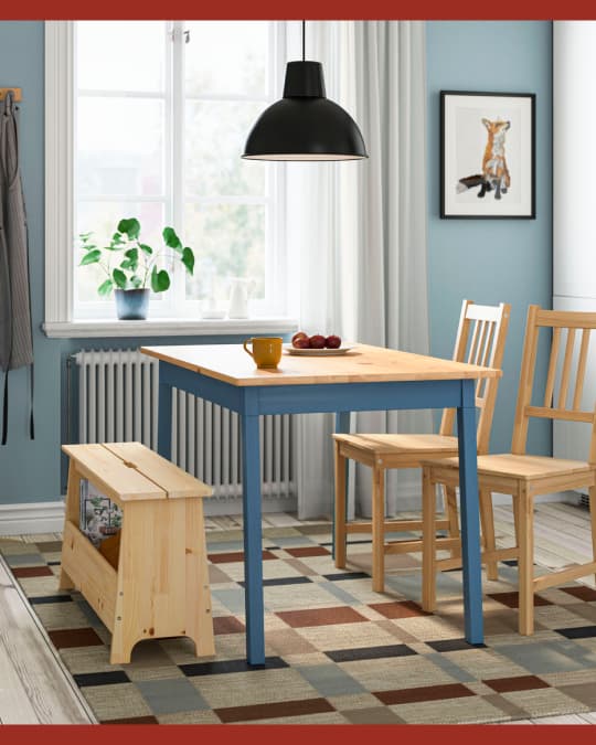 Un comedor de madera sobre una alfombra IKEA y en uno de los costados de la mesa una banqueta de madera larga.
