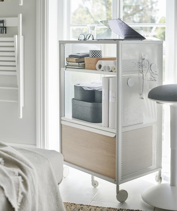 Un computer su un elemento contenitore con rotelle bianco e legno vicino alla finestra.