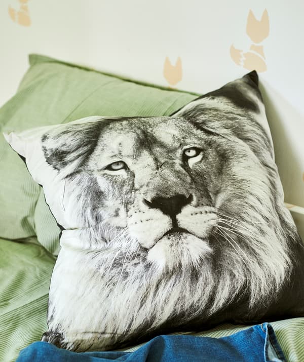 Un coussin avec une photo en noir et blanc d’un lion sur un lit avec du linge de lit vert. Le mur est peint au pochoir avec un motif de renard.