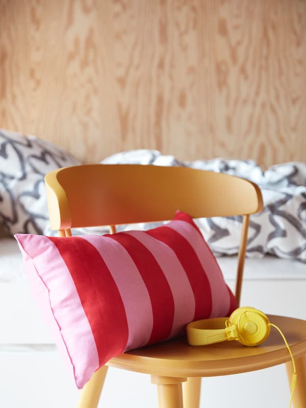 Un coussin rayé rose et rouge vif sur une chaise d’enfant jaune canari, avec un casque audio assorti.