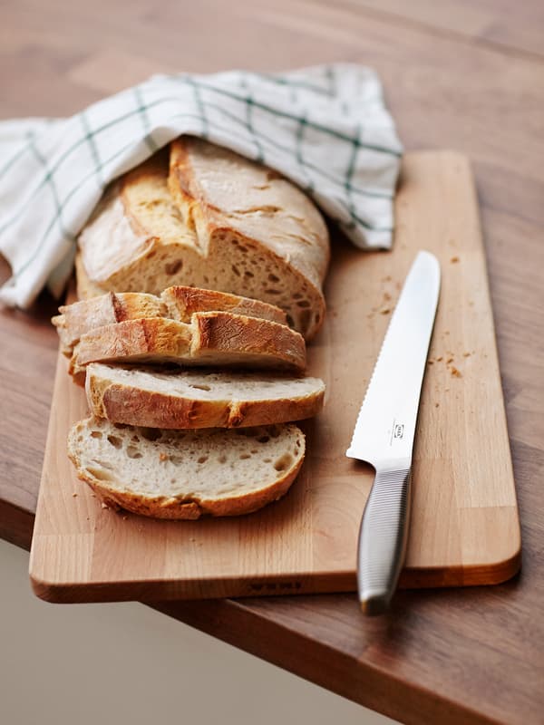 Un couteau à pain sur une planche à découper en bois à côté d’un pain dont quelques tranches ont été coupées