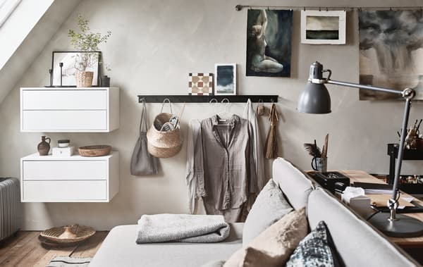 Un cuarto con teito inclinado con mobles de cores neutras, como por exemplo un sofá cama e un escritorio.