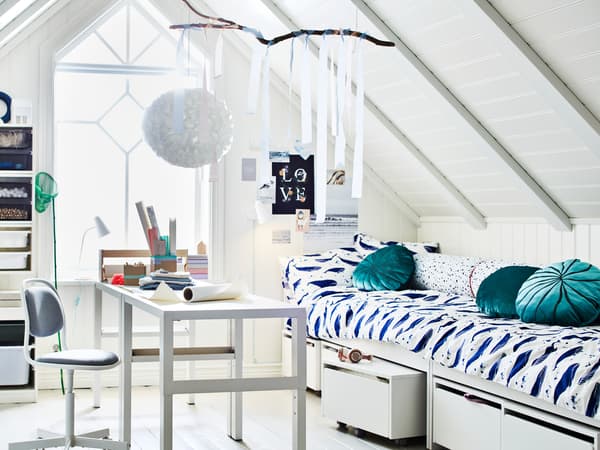 Un cuarto con teito inclinado e grandes fiestras. No medio da estancia hai dous escritorios PÅHL, preto de dúas camas e varias solucións de almacenaxe TROFAST.