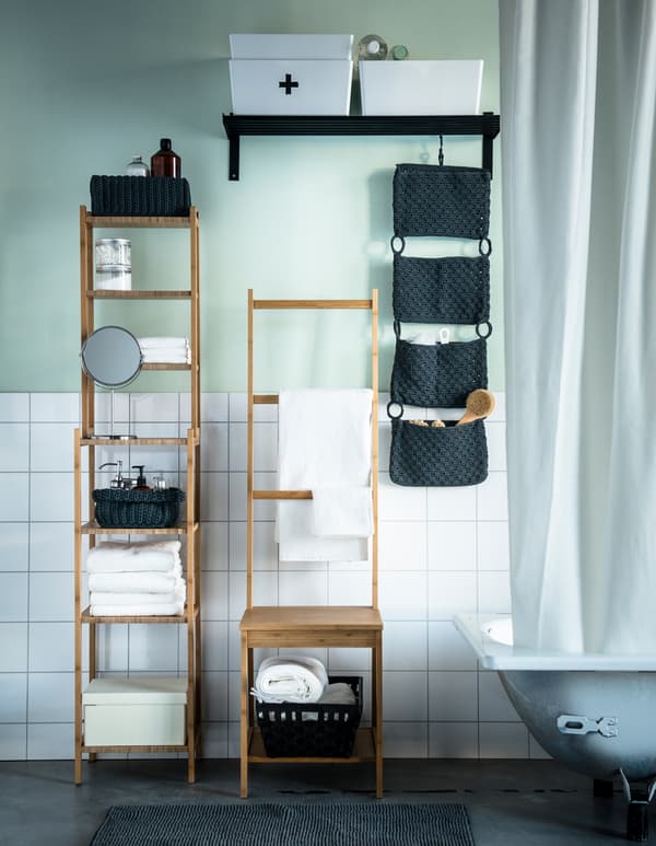 Un cuarto de baño con azulexos brancos e a parede en verde claro. Toallas e accesorios gardados en mobles de bambú.