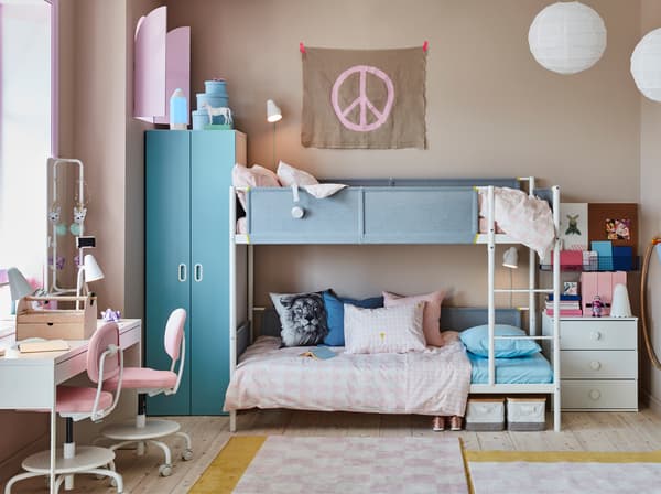 Un cuarto infantil para hermanos con una litera blanca, un escritorio compartido blanco y algunas sillas para escritorio rosas.