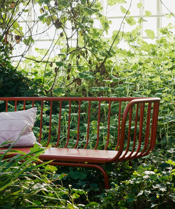 Un cuscino bianco su un divano da esterno rosso circondato da piante.