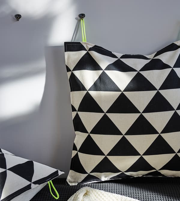 Un cuscino con una fodera a fantasia geometrica in bianco e nero appeso ad un gancio alla parete.