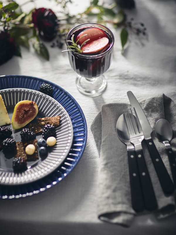 Un decor de masă elegant, inclusiv o față de masă albă, un preparat ușor pe o farfurie STRIMMIG și o băutură într-un pahar VARDAGEN.