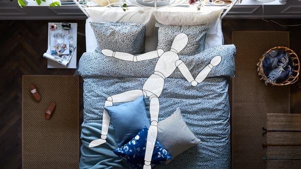 Un dibujo animado dibujo de una persona está durmiendo en una cama con ropa de cama LEIRVIK VATTENMYNTA. A cada lado de la cama hay una alfombra marrón.