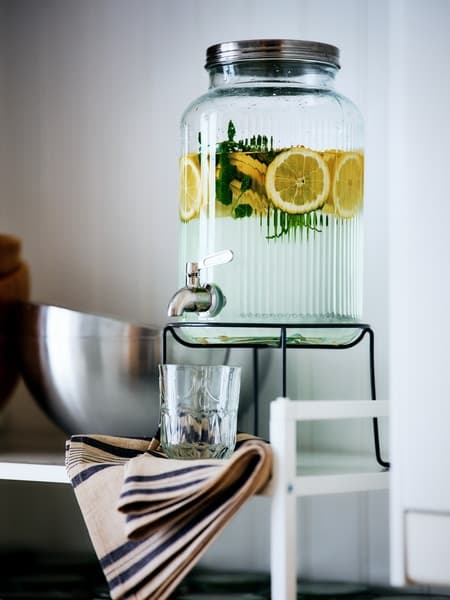 Un dispenser VARDAGEN pieno di acqua, menta e fettine di limone. Sotto, un bicchiere e accanto una ciotola in metallo BLANDA BLANK.