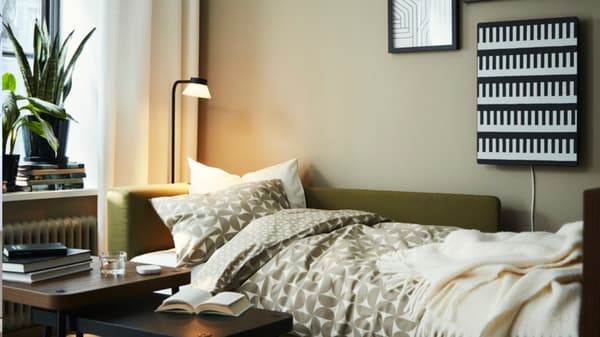 Un divano a letto a 2 posti grigio scuro SKÖNABÄCK aperto in un soggiorno ben illuminato.