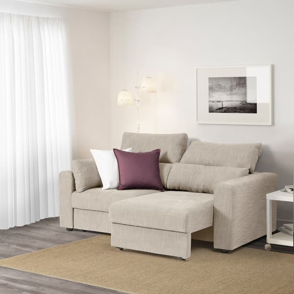 Un divano con poggiatesta regolabili e seduta ad estrazione ESKILSTUNA beige in un angolo di un salotto. Nel salotto ci sono un tappeto beige,un tavolino, un fotografia incorniciata e una tenda bianca.