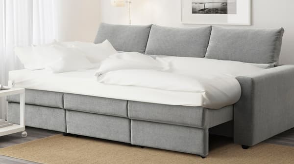 Un divano letto ESKILSTUNA aperto con cuscini e piumino bianco. Accanto al divano un tavolino bianco. 