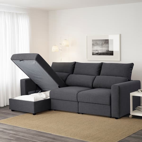 Un divano letto ESKILSTUNA con contenitore in un salotto. Una parte del divano è alzata e svela un piumino. 
