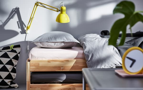 Un divano letto UTÅKER con alcuni cuscini grigi. Alla parete, una lampada gialla.