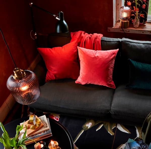 Un divano nero con due cuscini e un plaid rosso illuminato da una lampada a sospensione SOLKLINT.