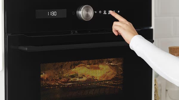 Un doigt touchant le panneau commande d'un micro onde fermé, avec à l'intérieur un plat