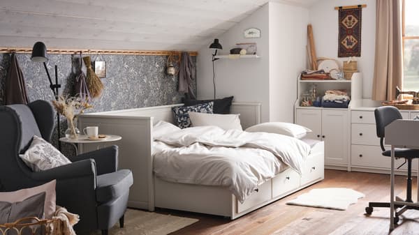Un dormitorio acogedor con un techo inclinado, un diván blanco con tres cajones y una combinación de almacenaje blanca.