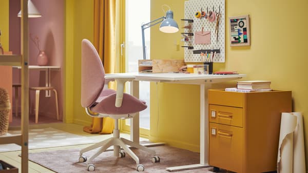 Un dormitorio color amarillo con un escritorio TROTTEN y al costado una cajonera.
