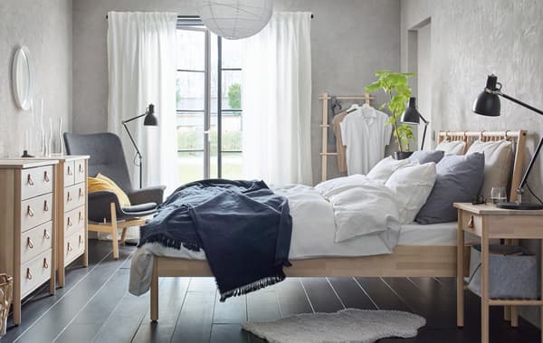 Un dormitorio con decoración en tons neutros cunha estrutura de cama de madeira, unha cómoda con caixóns e unha mesa de noite.