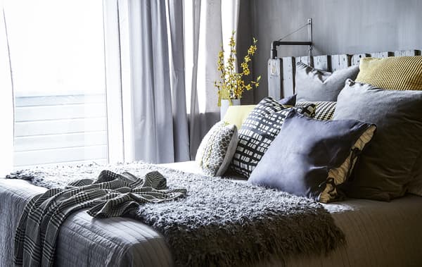 Un dormitorio con decoración gris e coxíns amarelos.