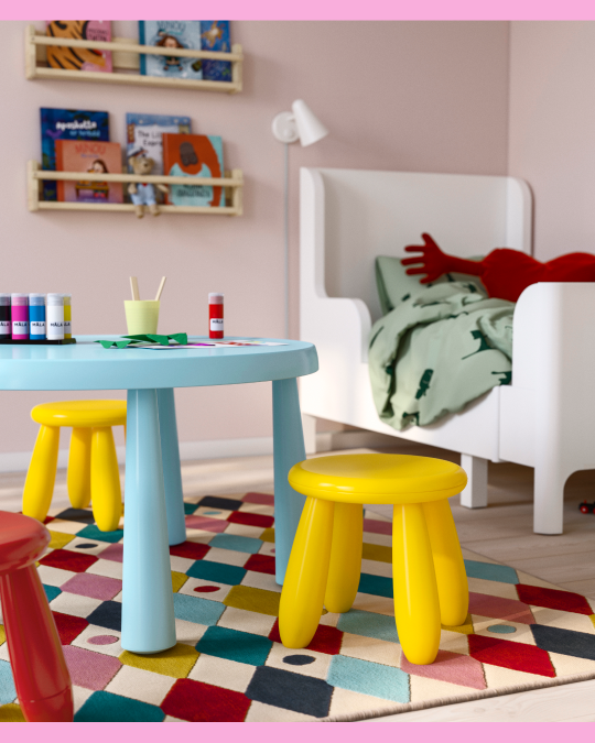 Un dormitorio infantil con mesas, butacos y camas para niños.