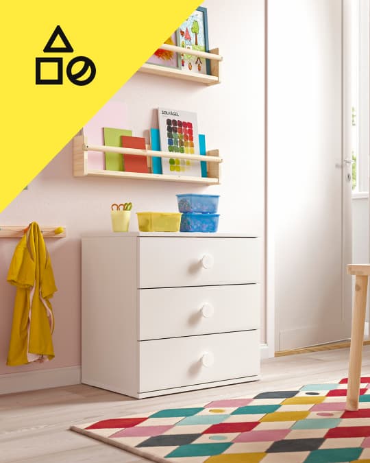 Un dormitorio infantil con un tapete de colores y una cómoda infantil blanca de tres cajones.