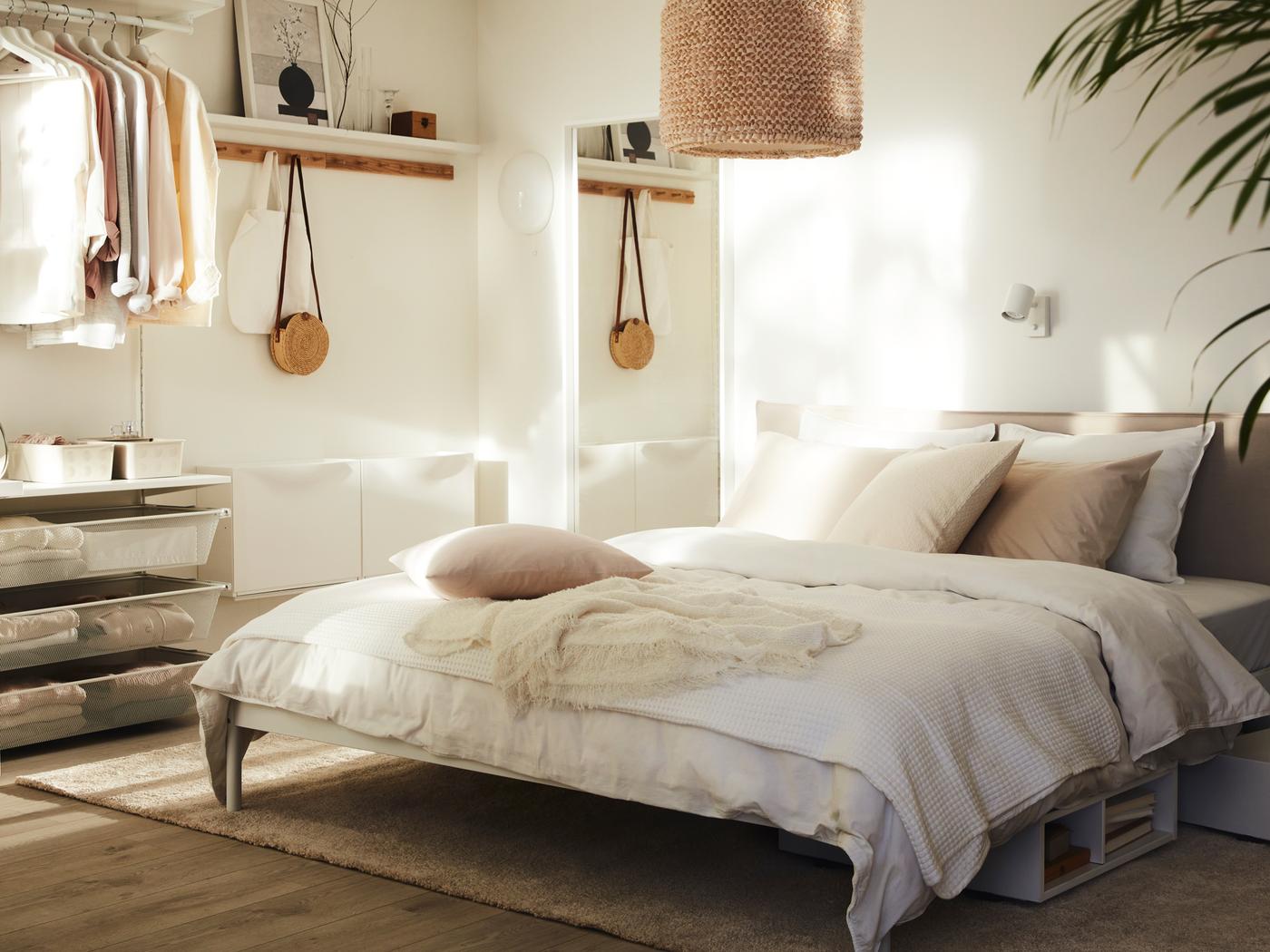 Un dormitorio soleado en tonos neutros con una cama KLEPPSTAD con ropa de cama de color claro y una pantalla de lámpara LERGRYN colgando sobre ella.