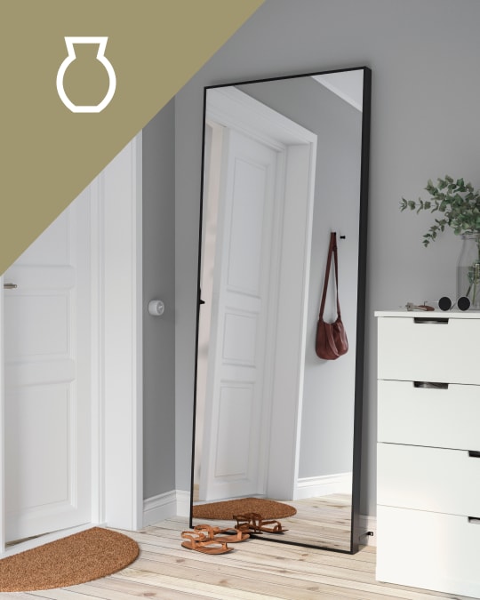 Un dormutorio con un espejo de cuerpo completo apoyado en la pared al costado de una cómoda.