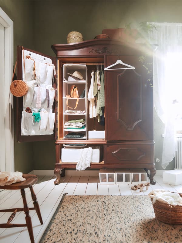 Un dulap din lemn în stil tradițional, cu ușa deschisă, lăsând să se vadă sistemul IKEA de organizare a hainelor din interior.