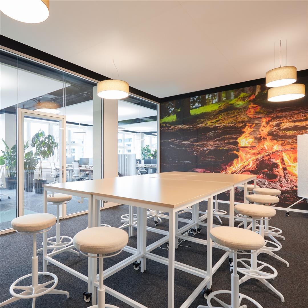 Un écran est posé sur un bureau blanc réglable en hauteur. Une lampe de bureau, elle aussi blanche et réglable, est installée à côté.