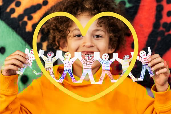 Un enfant souriant tient en guise de guirlande un découpage de petits personnages en forme de bâton aux couleurs vives.