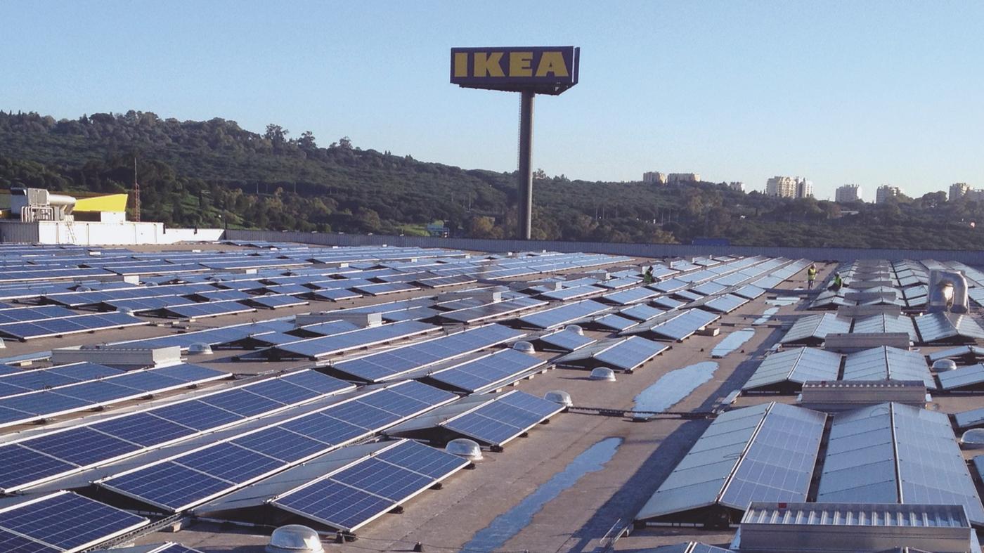Un ensemble de centaines de panneaux solaires sur le toit d'un bâtiment IKEA. À l'arrière-plan, une grande enseigne IKEA à trois faces.