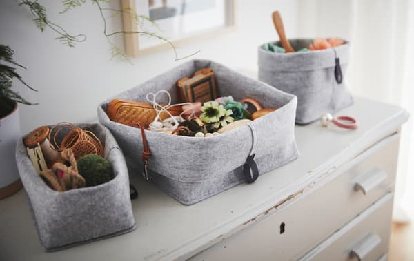 Un ensemble de paniers RAGGISAR en tissu remplis de babioles et de menus objets, posés sur une vieille commode usée.