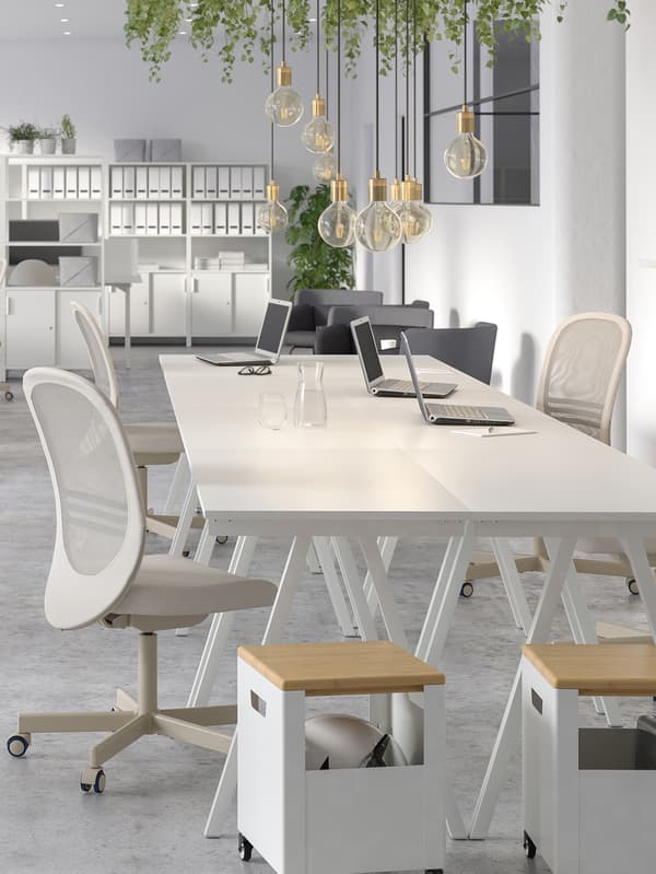 Un entorno de oficina grande, blanco y luminoso con sillas para conferencias, revisteros, plantas y escritorios TROTTEN blancos.