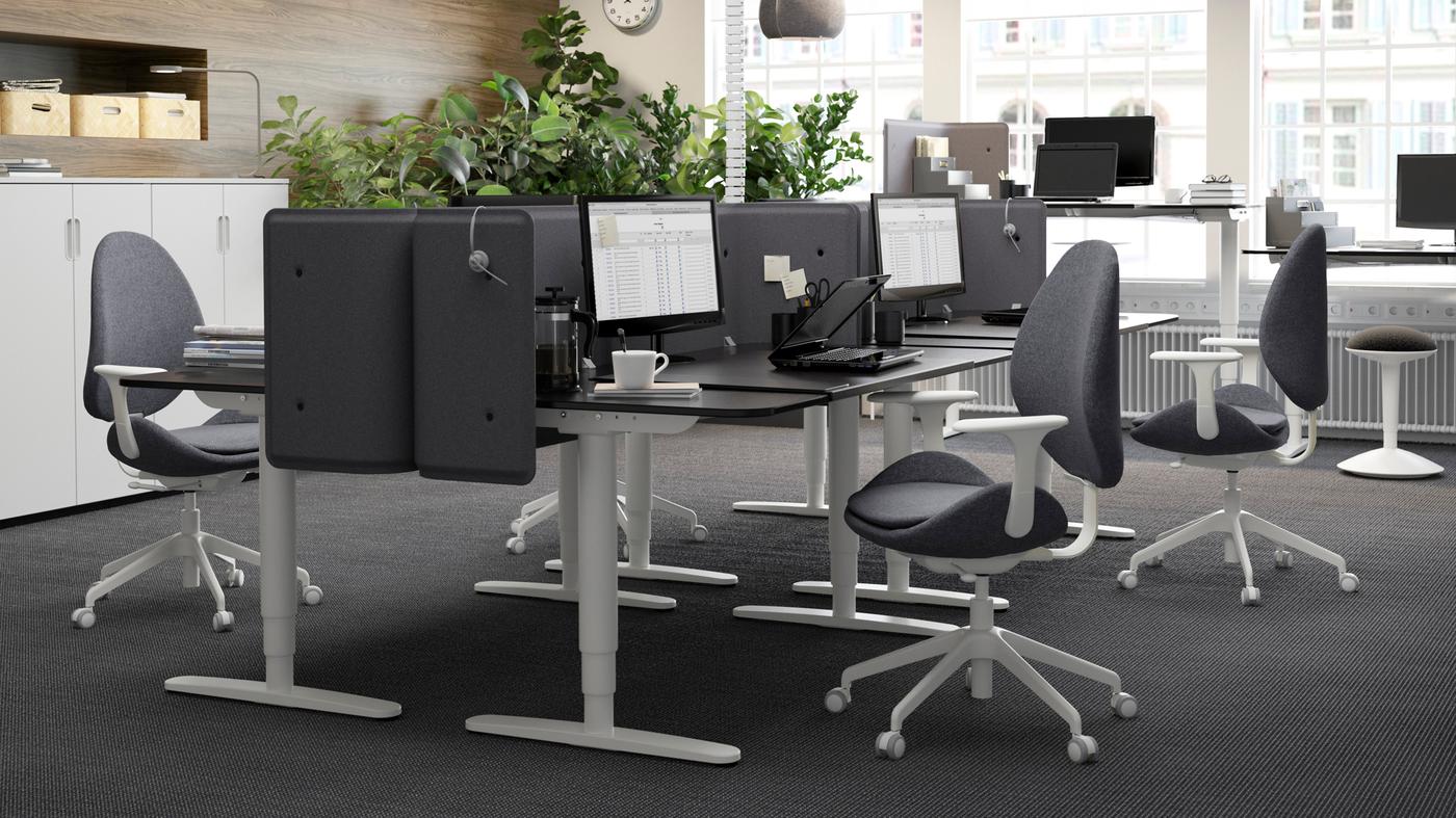 Un environnement de bureau noir et gris avec des bureaux assis-debout noirs et bruns BEKANT, face à face pour créer des cubicules.