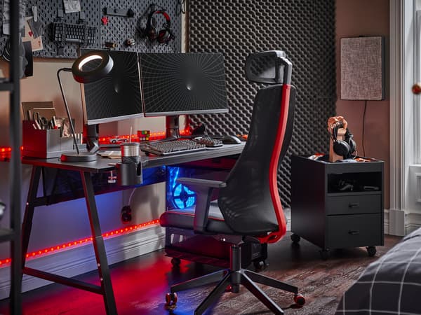 Un escriptori gaming UTESPELARE negre amb dues pantalles, una cadira gaming negra, una calaixera negra i uns quants accessoris gaming.