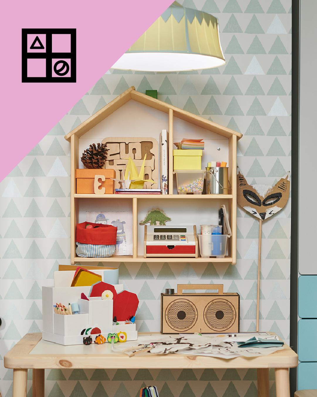 Un escritorio infantul y en la pared una repisa de madera en gorma de caja con juguetes en sus repisas. En la esquina superior de la imagen un triángulo rosa con figuras geométricas.