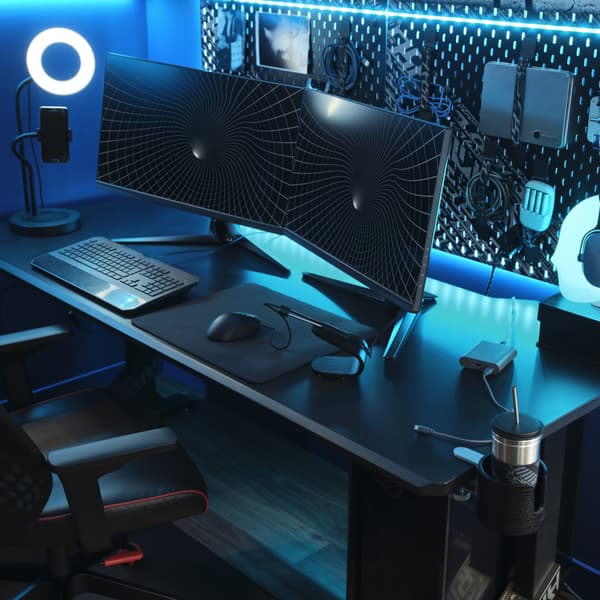 Un escritorio UPPSPEL con dos monitores instalados para jugar videojuegos, una silla gamer MATCHSPEL y accesorios gamer en un ambiente con luz azul. 