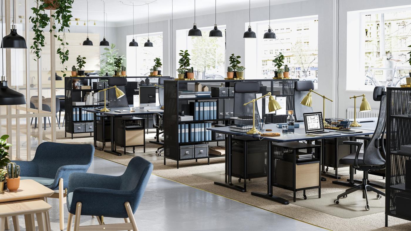 Un espace de bureau garni de plantes sur le dessus des étagères en filet noir et des bureaux assis-debout noirs BEKANT.