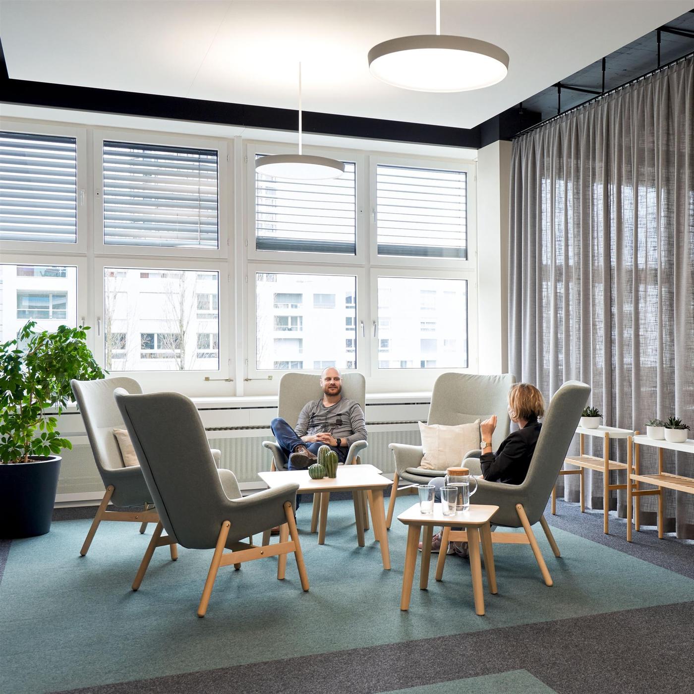 Un espace de discussion ouvert dans un bureau, composé de cinq sièges à dossier haut et d’une table basse au milieu pour une discussion informelle entre collaborateur-trice-s.