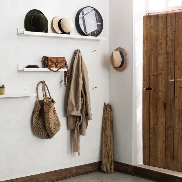 Un espace de porte avant avec des murs blancs, une porte en bois et des étagères murales qui portent des accessoires et des manteaux.