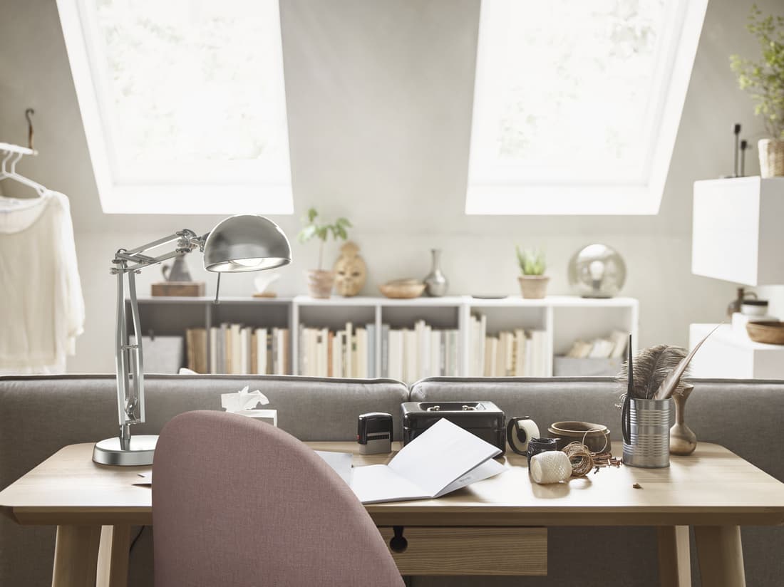 Un espace de travail à domicile avec un bureau LISABO en plaqué frêne derrière un canapé, une lampe de bureau FORSÅ et une chaise pivotante GUNNARED.