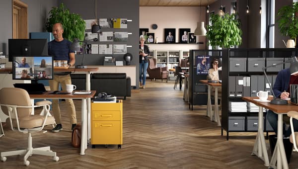 Un espace de travail avec des bureaux assis/debout IDÅSEN de couleur beige, des chaises pivotantes et divers caissons à tiroirs avec diverses personnes au travail.