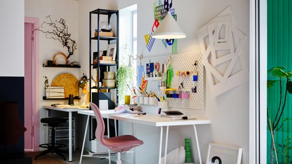 Un espace de travail avec une table LAGKAPTEN/TILLSLAG blanche, une chaises de bureau LÅNGFJÄLL brun clair-rose et des panneaux perforés et une suspension.